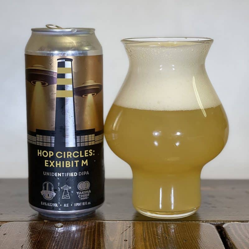 Glass filled with beer sitting next to a can of BlackStack Brewing Hop Circles: Exhibit M on a table.