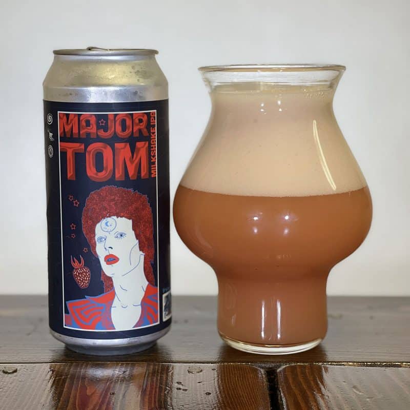 Glass of reddish beer next to a can of Eagle Park Brewing Major Tom Milkshake IPA.