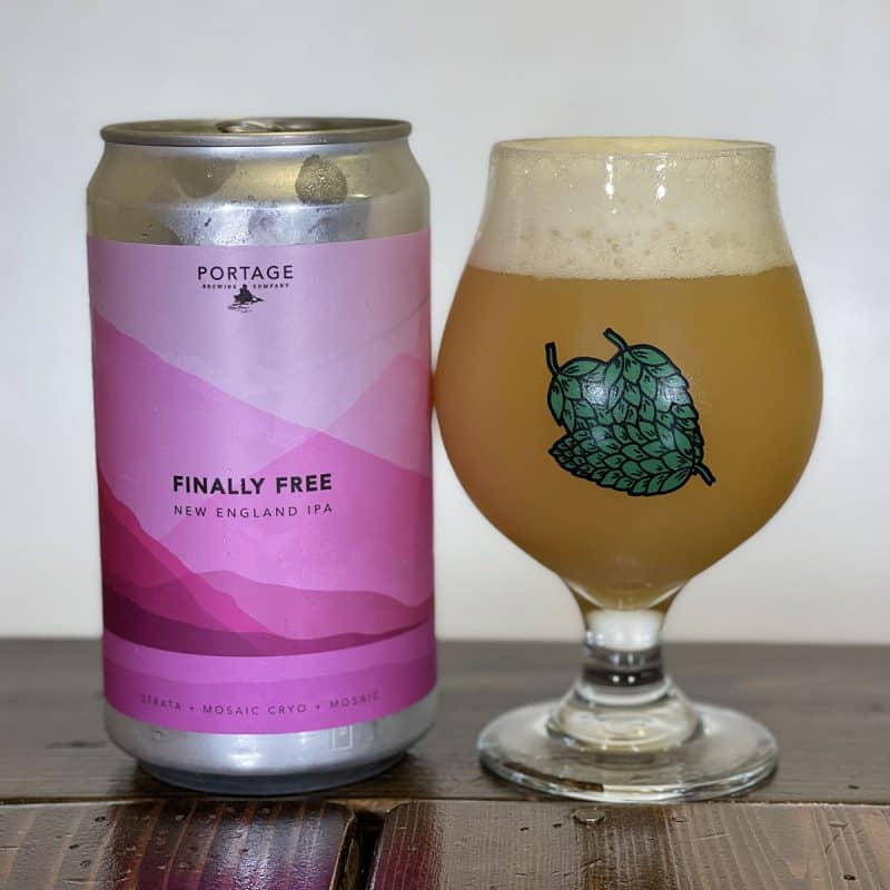 Crowler of Portage Brewing Finally Free New England IPA sitting next to a snifter glass filled with the beer.