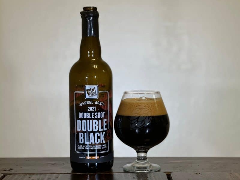 Bottle of Bent Paddle Brewing Double Shot Double Black 2021 sitting next to a snifter glass of dark beer.