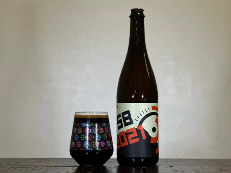 Glass of dark beer next to a bottle of Fair State Co-op FSB 2021.