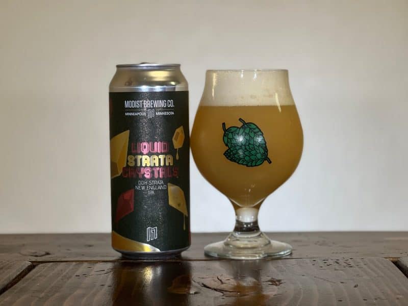 Can of Modist Brewing Liquid Strata Crystals and a snifter glass filled with beer.