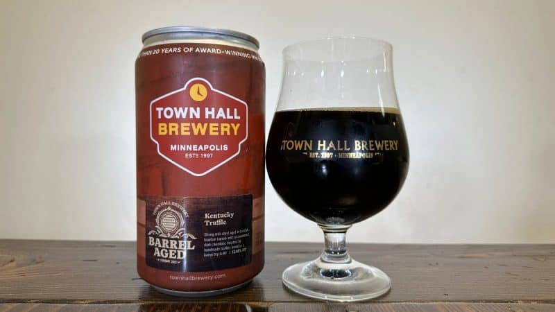 Crowler of Town Hall Brewery Kentucky Truffle 2023 next to a snifter glass filled with dark beer on a wood table.