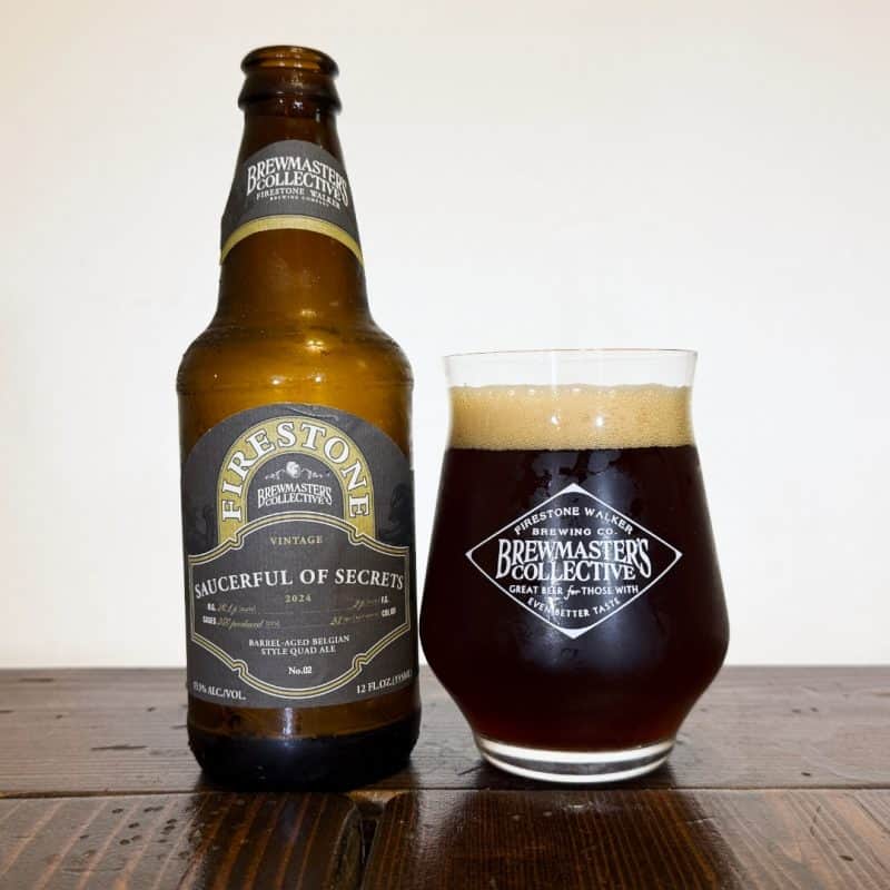 Bottle of Firestone Walker Brewing Saucerful Of Secrets next to a glass of dark honey-colored beer.