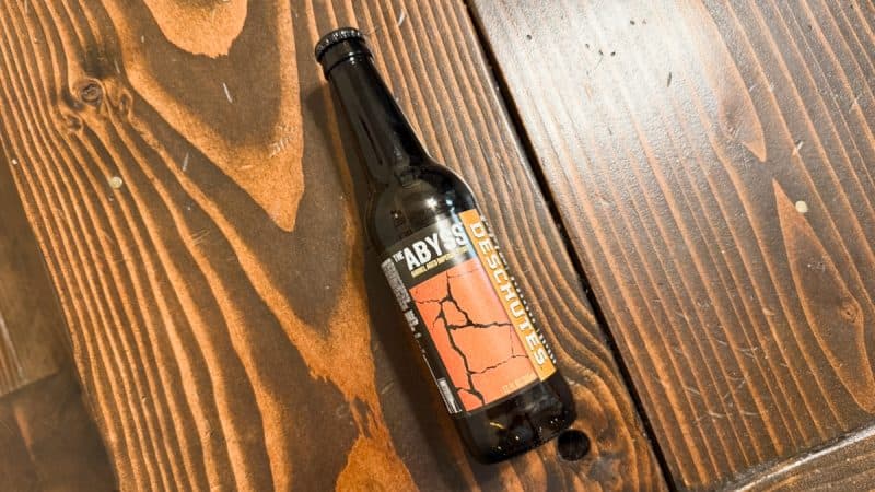 Bottle of Deschutes Brewery The Abyss 2025 laying on a wood table.