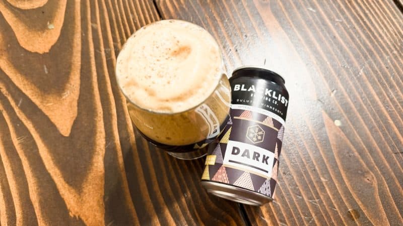 Can of Blacklist Brewing Dark Imperial Stout laying next to a glass of beer.