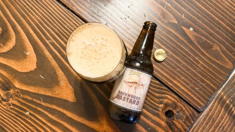 Bottle of Founders Brewing Backwoods Bastard 2025 and a snifter filled with beer, sitting on a wood table.