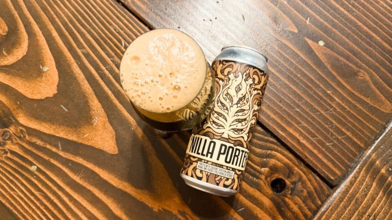 Can of Lulupin Brewing 'Nilla Porter laying next to a glass of foamy beer on a wooden table.